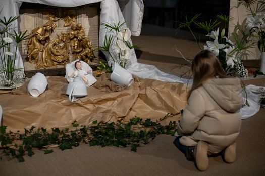A girl looks at christmas creche with Joseph Mary and small Jesus