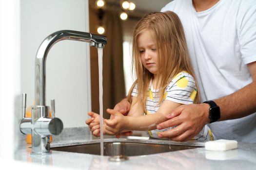 Father and daughter washing their hands above the sink in a kitchen at their home