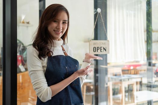 Portrait of a smiling Asian entrepreneur standing behind her cafe counter with open sign board.