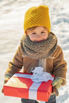 Happy winter child boy hold gift on snow background. Cute boy in winter clothes hat and scarf close up. Winter family holidays concept