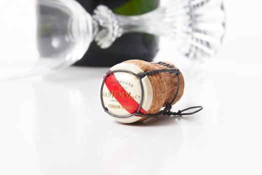 IRVINE, CALIFORNIA - AUGUST 12, 2019: G. H. Mumm Champagne cork closeup on white with reflection, a bottle and flute are in the background out-of-focus.