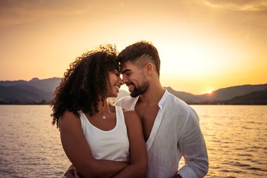 Romance scene of multiracial stylish couple in love looking in eyes head to head at sunset with sun setting among mountain in background. Handsome guy in white shirt flirting with Hispanic girlfriend