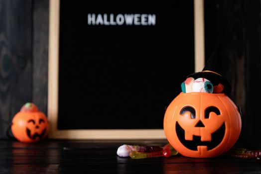 Halloween concept. Halloween party jack o lanterns pumpkins full of sweets on black wooden background, blurred letter board with words Halloween on background