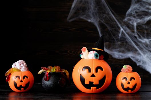 Halloween concept. Halloween party jack o lanterns pumpkins full of sweets on black wooden background with spider web
