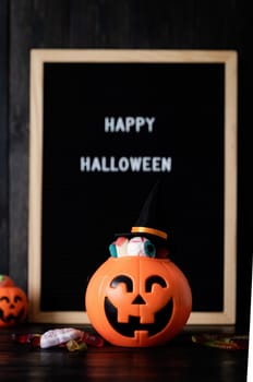 Halloween concept. Halloween party jack o lanterns pumpkins full of sweets on black wooden background, blurred letter board with words Happy Halloween on background