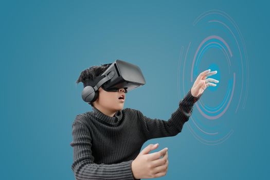 Asian boy wearing VR glasses headset with technology graphics in front on blue color background.