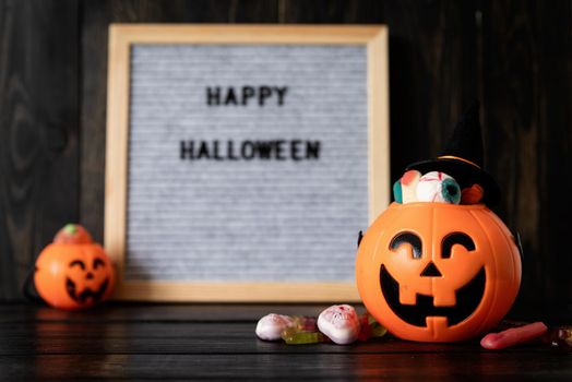 Halloween concept. Halloween party jack o lanterns pumpkins full of sweets on black wooden background, blurred letter board with words Happy Halloween on background