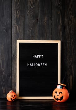 Halloween concept. Halloween party jack o lanterns pumpkins full of sweets on black wooden background, letter board with words Happy Halloween
