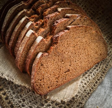 Fresh rye sliced bread on natural linen napkin on rustic wooden background