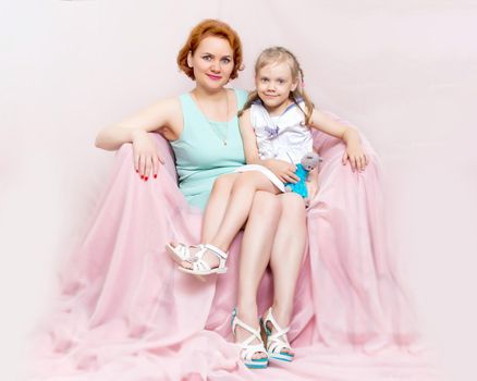 Mom and daughter are sitting on the couch. The concept of family happiness, parenthood, childhood. Isolated on white background.