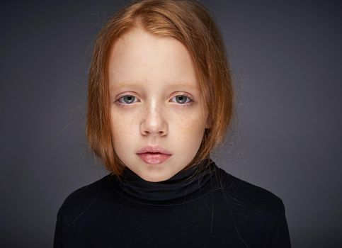 red-haired girl with freckles on her face in a black sweater posing. High quality photo