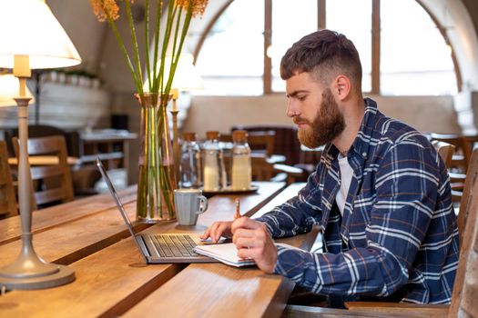 Casual business man or freelancer planning his work on notebook, working on laptop computer with smart phone, cup of coffee on table at coffee shop or home office, working from cafe concept