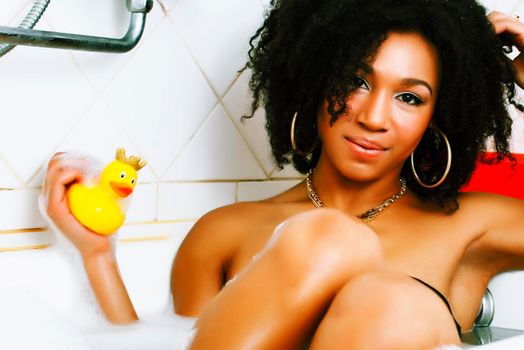 young afro-american teen girl laying in bath with foam, wearing swag jewelry flawless, making selfie close up
