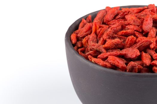 Chinese goji berries in dark stone bowl close up on white background