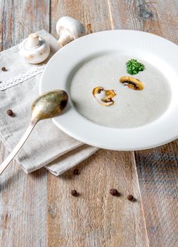 Delicious creamy mushroom soup with some pieces of mushrooms in it, old spoon and napkin