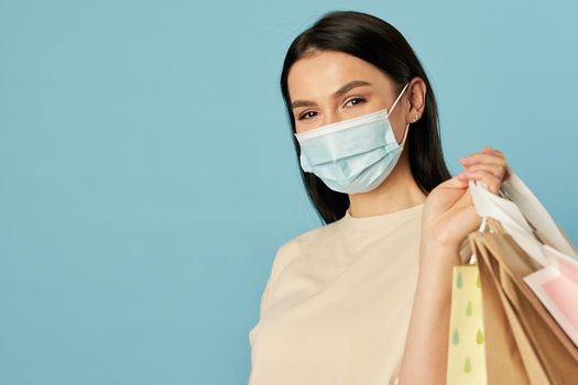 Waist up of pretty woman in disposable face mask holding shopping bags. Copy space. Quarantine, coronavirus concept