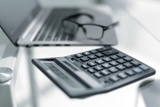 Close up detail view of a white work desk with a laptop computer and a calculator with numbers on the screen.