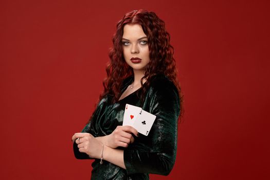 Young sexy woman with a red curly hair, holding aces in her crossed hands, on a red background. Poker