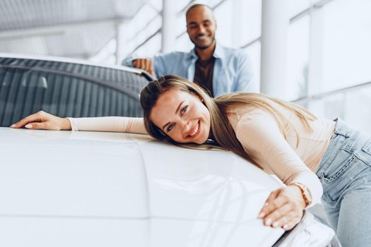 Young couple man and woman hugging their new car in a car shop close up