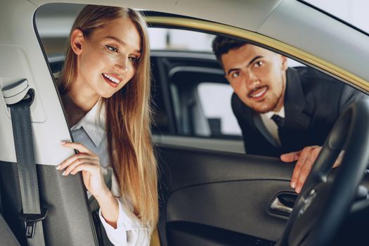 Man car dealer showing a woman buyer a new car in car salon