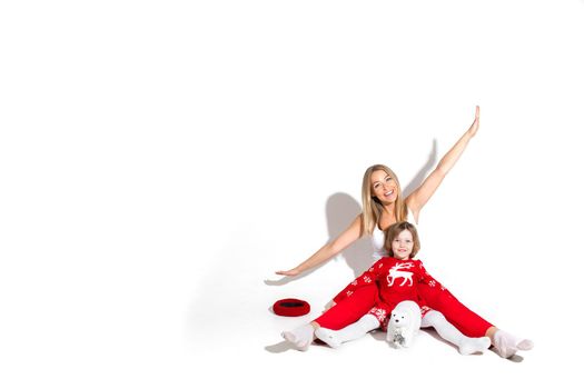 Studio photo of jovial mother with outstretched arms with daughter in front of her sitting on the floor.