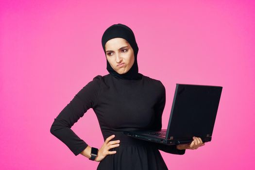 muslim woman in hijab with laptop technology learning pink background. High quality photo