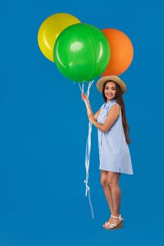 Full-length shot of smiling young woman looking camera and holding colorful air balloons isolated over blue. Conception of celebrations and birthday party