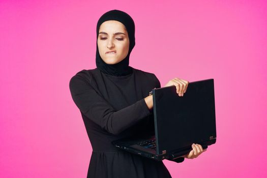 muslim woman in hijab with laptop technology learning pink background. High quality photo