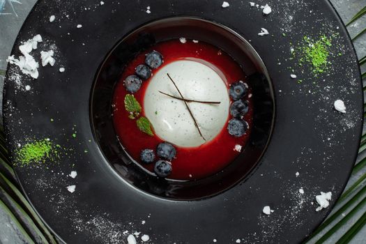 Panna cotta with raspberry sauce in a black plate.