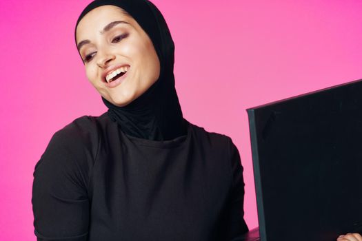 muslim woman in hijab with laptop technology learning pink background. High quality photo