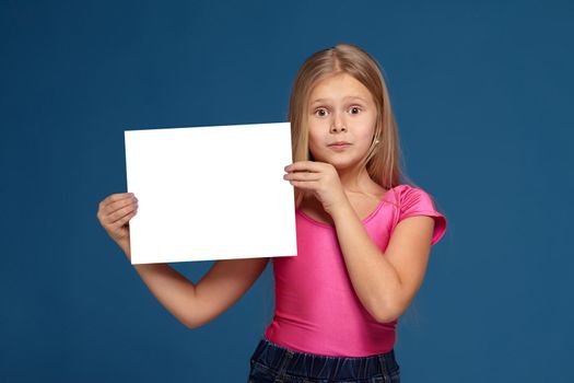 Portrait of adorable blonde little girl on blue background. in pink shirt, holding horizontal white copy space