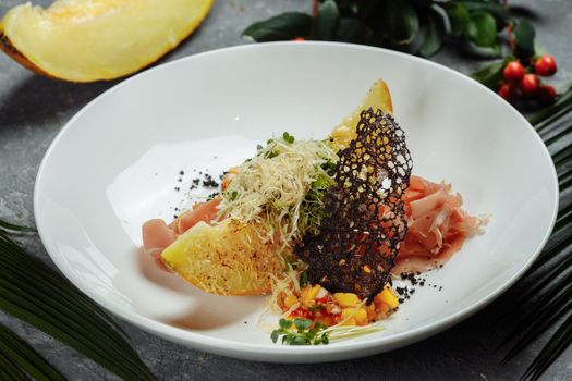 baked melon with parmesan and jamon on a white plate.