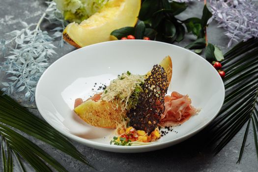 baked melon with parmesan and jamon on a white plate.