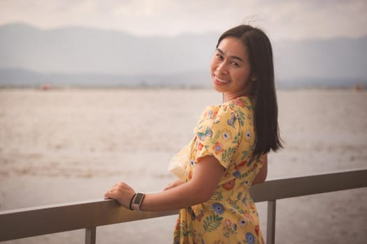 Asian woman tourist enjoying the view and smiling happily to the camera by the lake in vintage tone. Outdoor travel and Nature theme.