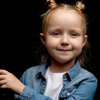 Beautiful little girl, studio portrait on a black background. The concept of a happy childhood, style and fashion.