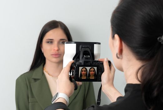 Doctor taking picture of young female patient before aesthetic treatment on white background with 3d camera system