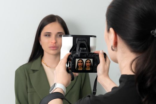 Doctor taking picture of young female patient before aesthetic treatment on white background with 3d camera system