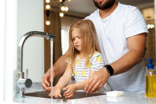 Father and daughter washing their hands above the sink in a kitchen at their home