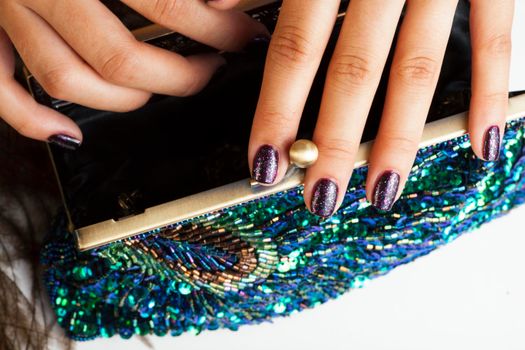 woman hands with shiny manicure holding little purse peacok feather, cosmetic and fashion people concept close up