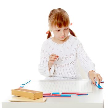 A little girl in Montessori kindergarten sits at a table and studies Montessori stuff. The concept of school and preschool education, harmonious development of the child. Isolated on white background.