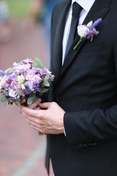 Caucasian groom wearing black suit and tie keeping bouquet of flowers. Concept of wedding.