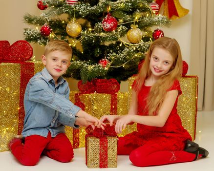 Boy and girl near the Christmas tree decorated with toys and gifts on Christmas Eve. Holiday concept.