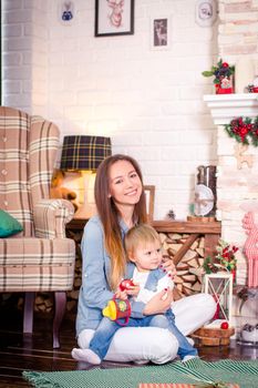 Young mother sitting with little daughter in decorated room for Christmas. Concept of celebrating New Year and winter vacations.