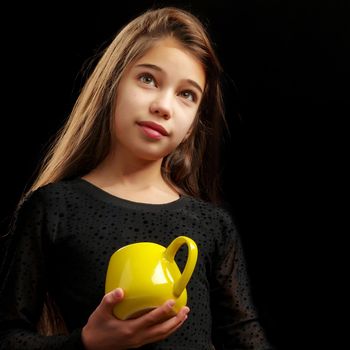 Beautiful little girl with a mug. Studio portrait on black background.