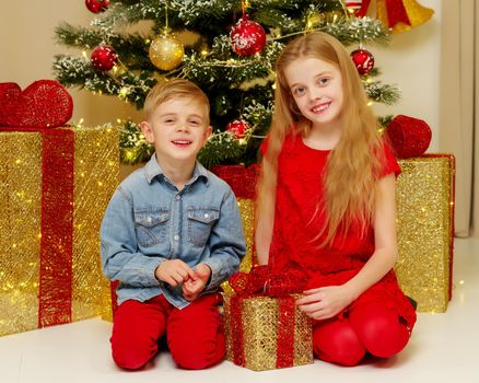 Boy and girl near the Christmas tree decorated with toys and gifts on Christmas Eve. Holiday concept.