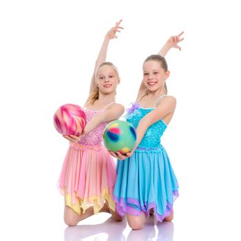 Two cheerful little girls gymnasts in competitions, perform exercises with the ball. The concept of children's sports, fitness, healthy lifestyle. Isolated on white background.