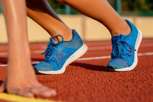 Close-up of woman's legs in blue sneakers on start before jogging. Red treadmill at the stadium