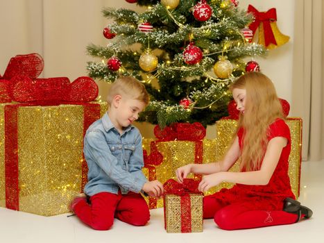 Boy and girl near the Christmas tree decorated with toys and gifts on Christmas Eve. Holiday concept.