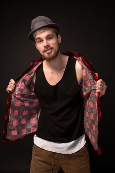 Handsome trendy young guy at the studio on black background. He wears beard and a plaid shirt. Belt portrait