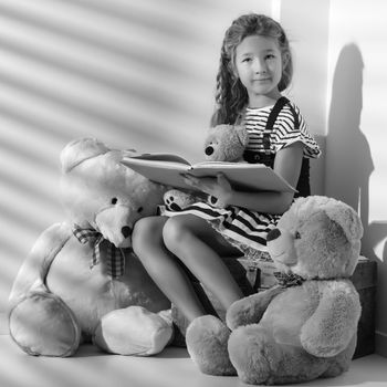 Cute little girl is reading a book to a teddy bear. Black and white photo. The concept of the game, family happiness.